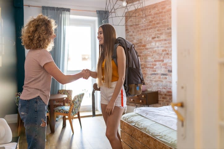 a-woman-shakes-hands-with-a-younger-woman-wearing-a-backpack-as-they-stand-in-a-studio-rental-room