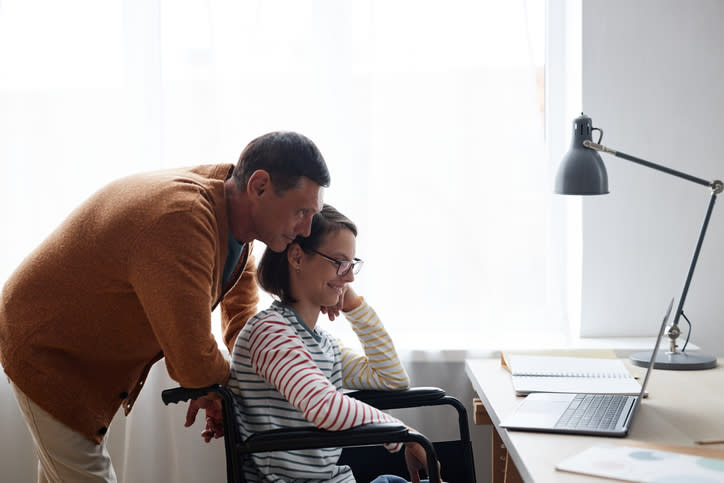 A teenager with a disability studying online with the help of her father.

