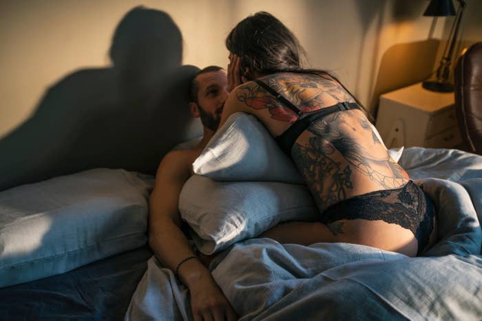 A couple embracing on a bed with the focus on a woman's back with a tattoo