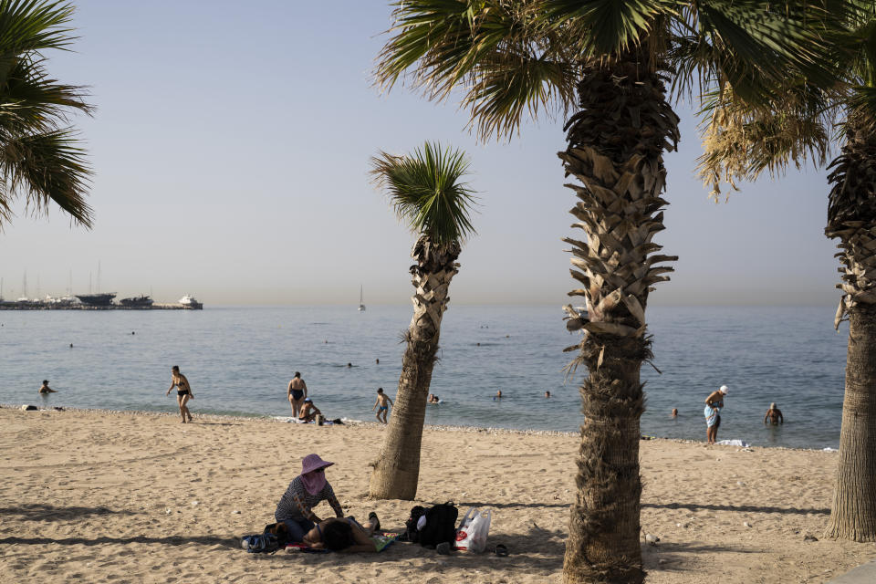 A woman gives massage to a bather in the shade of a tree during a hot day at Alimos beach near Athens, Friday, July 14, 2023. Temperatures were starting to creep up in Greece, where a heatwave was forecast to reach up to 44 degrees Celsius in some parts of the country over the weekend. (AP Photo/Petros Giannakouris)