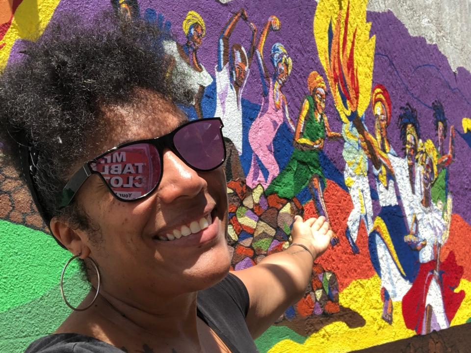 A woman taking a selfie points toward a mural on the street in Philipsburg.