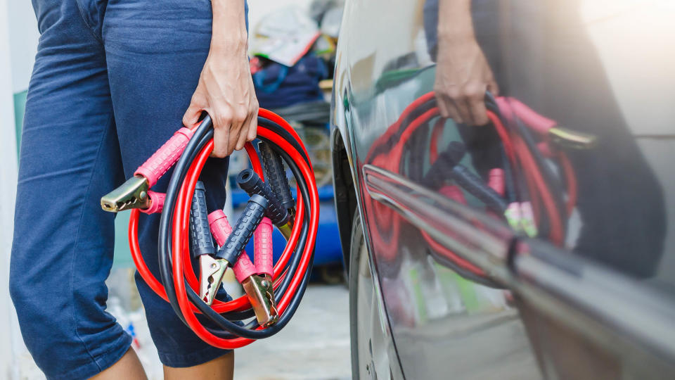 Someone carrying jumper cables next to a car