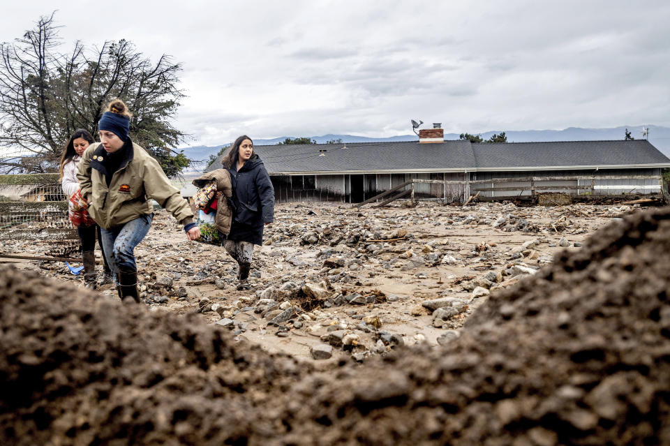 Hana Mohsin, right, carries belongings from a neighbor's home which was damaged in a mudslide on Wednesday, Jan. 27, 2021, in Salinas, Calif. The area, located beneath the River Fire burn scar, is susceptible to landslides as heavy rains hit hillsides scorched during last year's wildfires. (AP Photo/Noah Berger)