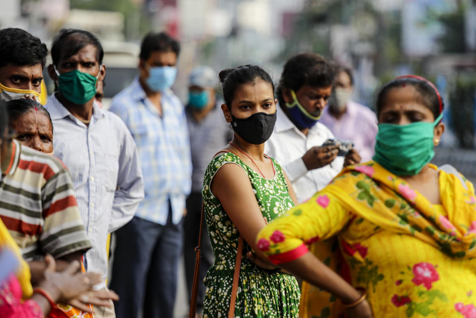 Commuters with face mask to prevent the spread of the coronavirus wait for a bus in Kolkata, India, Saturday, Oct. 10, 2020. India's total coronavirus positive cases near 7 million with another 73,272 infections reported in the past 24 hours. The Health Ministry on Saturday put the total positive caseload at 6.97 million, second to 7.66 million infections registered in the worst-hit United States. (AP Photo/Bikas Das)