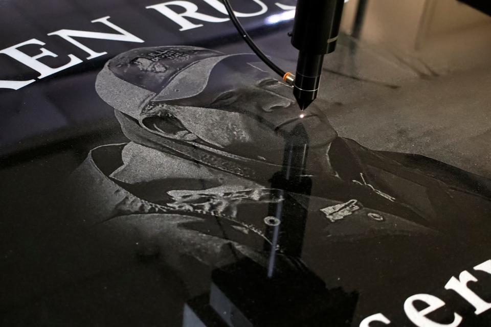 A laser etches an image of long-time Illinois Department of Natural Resources Fisheries Biologist Ken Russell onto a monument being constructed at Lacky and Sons Monument. The monument was dedicated at the Lake Story boat ramp near US 150 during the annual fishing derby.