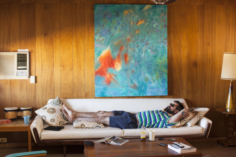 Man relaxing on a sofa with an abstract painting above and a glass on the side table
