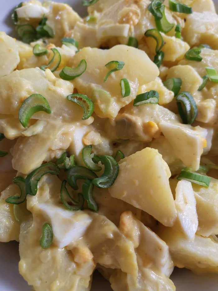 A close-up of a potato salad with slices of boiled potatoes, chopped green onions, and eggs mixed in a creamy dressing