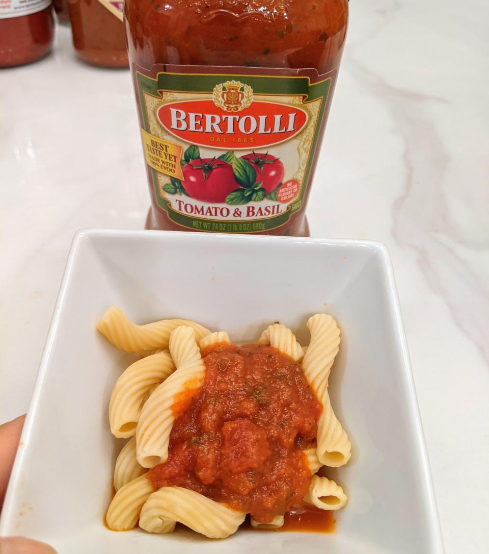 Jar of bertolli red sauce behind a small white bowl of pasta