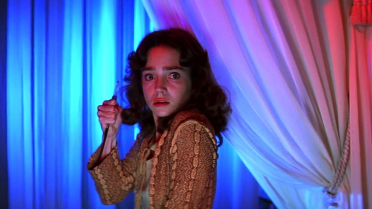 a ballet student holds a knife while standing in front of colorful curtains in a scene from 'suspiria,' a good housekeeping pick for best halloween movies