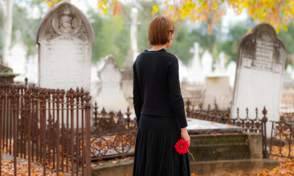 Young woman in mourning walking in cemetery in fall with red flower