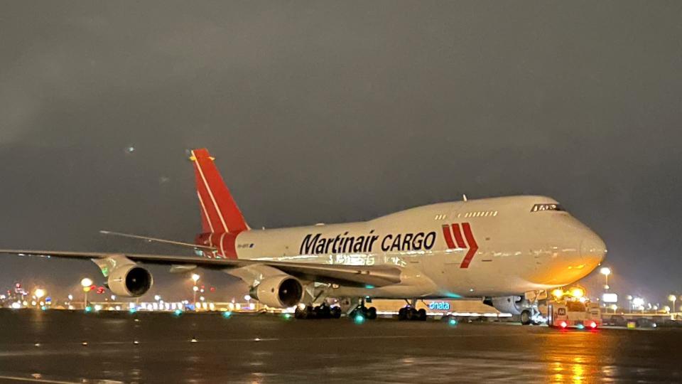 A Martinair Cargo jumbo jet with red tail moves along runway at night.