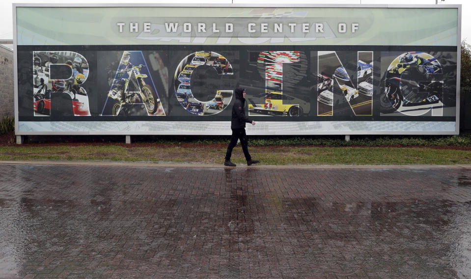 A pedestrian passes a billboard in the fan zone during the IMSA 24-hour race after it was red-flagged because of rain at Daytona International Speedway, Sunday, Jan. 27, 2019, in Daytona Beach, Fla. (AP Photo/John Raoux)