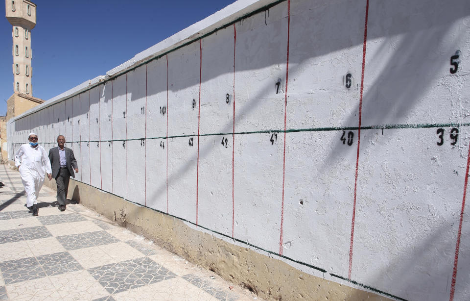 Men walk by a wall where electoral posters for the upcoming parliamentary elections will be placed, Thursday, May 20, 2021 in Ain Ouessara, 200 kilometres (125 miles) south of Algiers. Initially planned for April 22, the the legislative election will take place on June 12, 2021 in the North African country. (AP Photo/Fateh Guidoum)