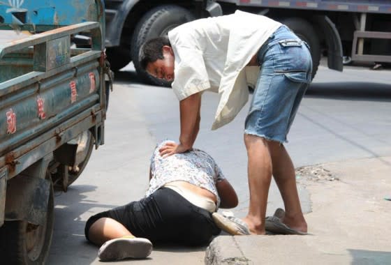 The man pins her down to the kerb of the road. (Photo: chinaSMACK.com)