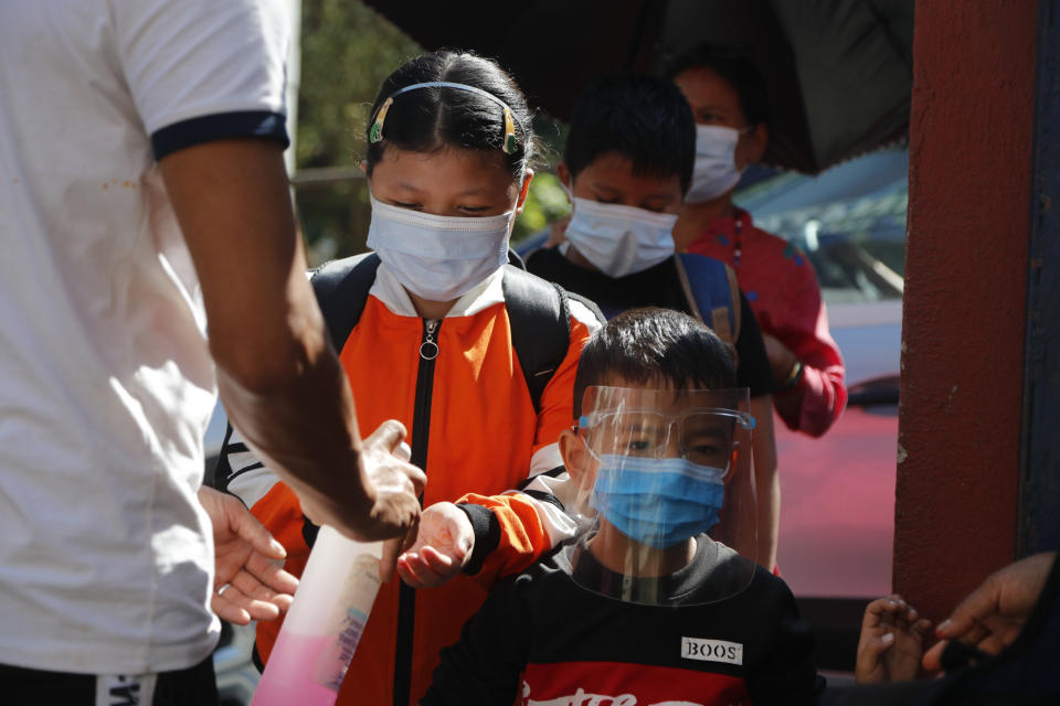 A door man gives hand sanitizer as Nepalese children arrive at their school that reopened after being closed for months due to the COVID-19 pandemic in Kathmandu, Nepal, Monday, Sept. 27, 2021. (AP Photo/Niranjan Shrestha)