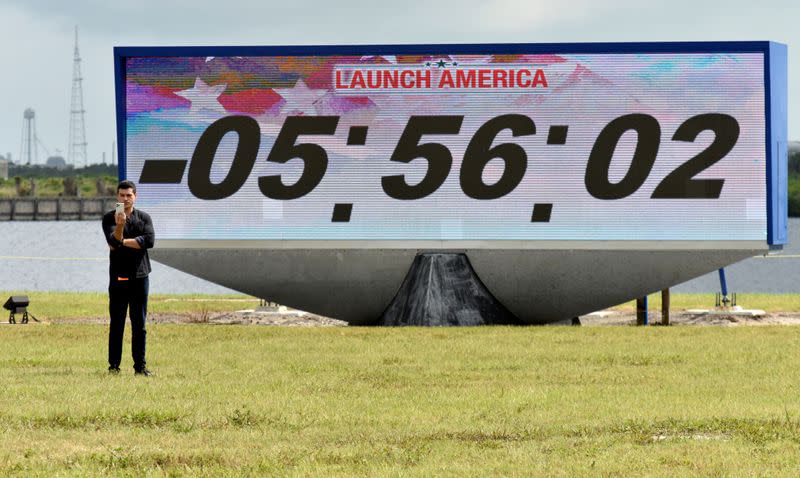A reporter does a stand-up in front of the countdown clock the press site before the launch of the SpaceX Crew Dragon on a Falcon 9 booster rocket from Pad39A