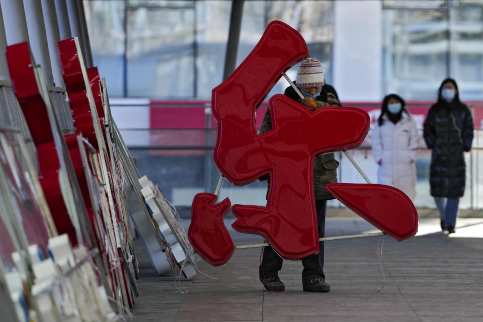 A worker wearing a face mask to help protect from the coronavirus carries characters reading "Happiness" for an installation for the upcoming Chinese Lunar New Year on a pedestrian bridge in Beijing, Tuesday, Jan. 25, 2022. (AP Photo/Andy Wong)