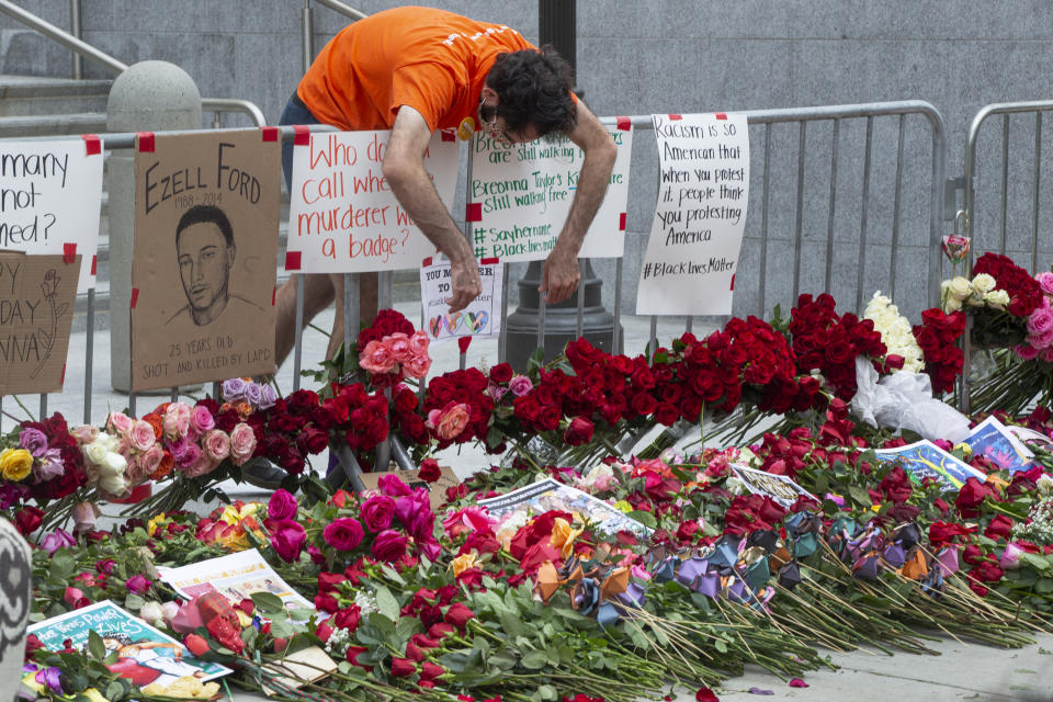 A man bends over a place full of flowers laid down by protesters outside the Hall of Justice, Friday, June 5, 2020, downtown Los Angeles. The protests sparked by the death of George Floyd, who died May 25 after he was restrained by Minneapolis police. (AP Photo/Damian Dovarganes)