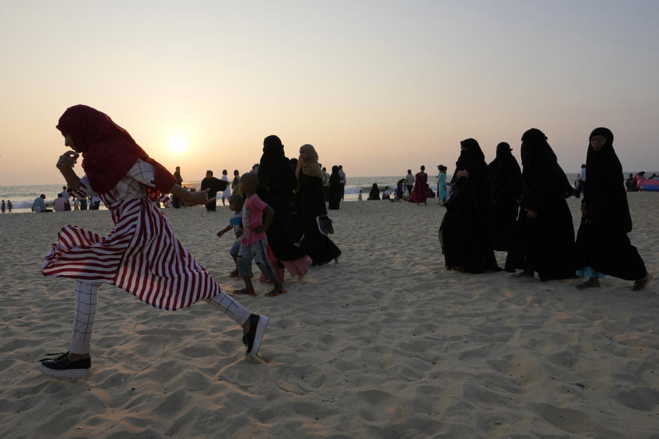 An Indian Muslim girl wearing a hijab runs past others wearing burqas during an evening at a beach in Udupi, Karnataka state, India, Feb. 25, 2022. The hijab is worn by many Muslim women to maintain modesty or as a religious symbol, often seen as not just a bit of clothing but something mandated by their faith. Opponents consider it a symbol of oppression, imposed on women. Hijab supporters deny that and say it has different meanings depending on the individual, including as a proud expression of Muslim identity. (AP Photo/Aijaz Rahi)