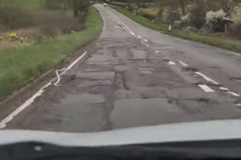 A606 Melton Road between Widmerpool Island and Hickling Pastures, as seen through windscreen of car from passenger seat, with loads of potholes and grass and trees on either side