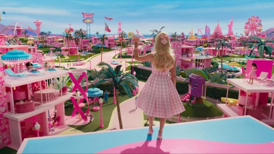 Barbie stands with her back facing us as she waves at all the Barbieland dream houses