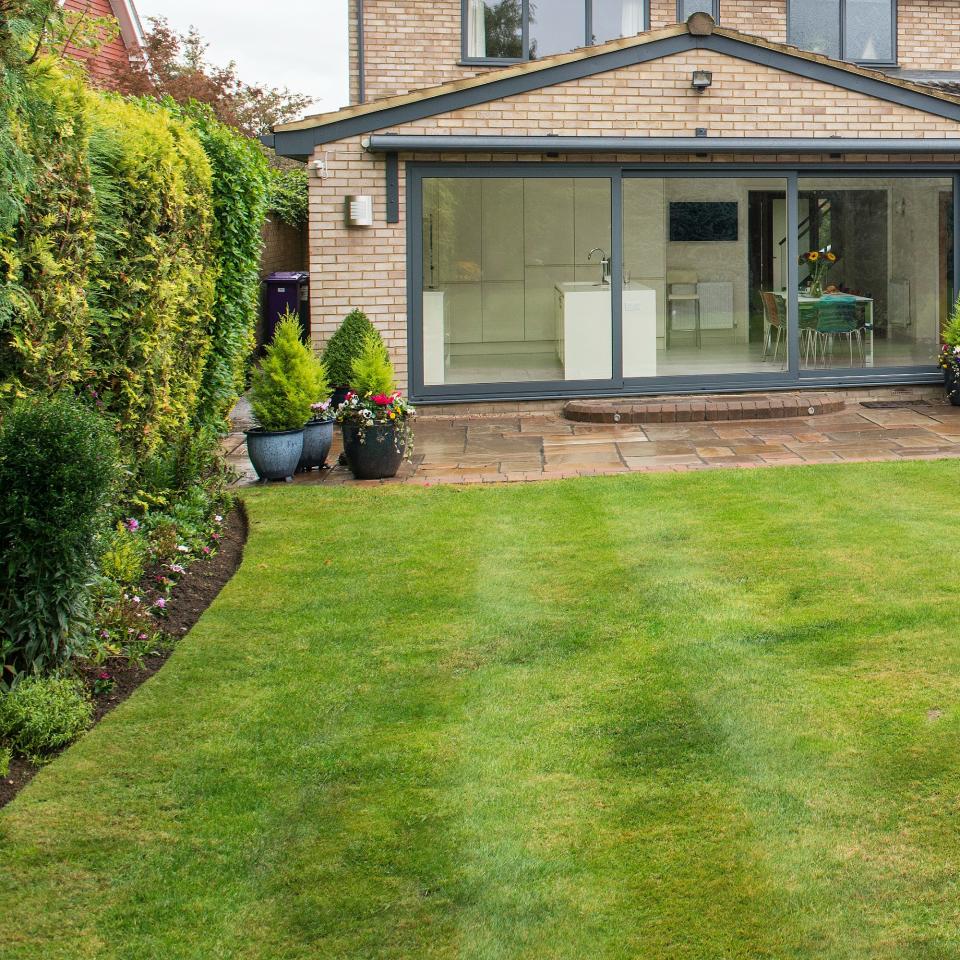 A back garden with a green lawn and a view of the back of the house and the kitchen