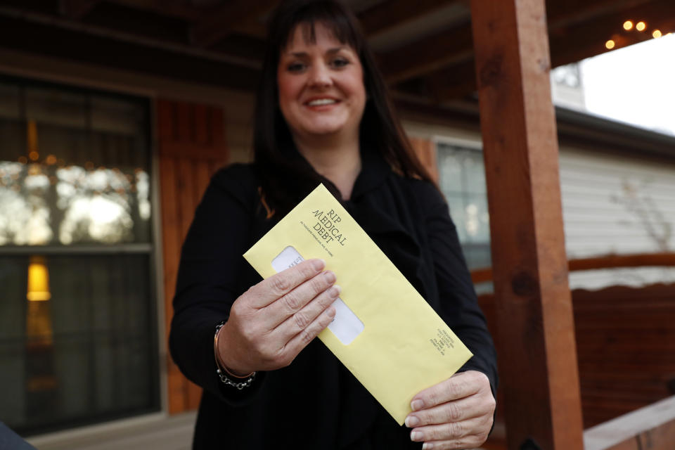 In this Dec. 20, 2018 photo, Reagen Adair holds on to an RIP Medical Debt yellow envelope as she poses for a photo at her home in Murchison, Texas. The co-founders of RIP Medical Debt buy millions of dollars in past-due medical debt for pennies on the dollar. But instead of hounding people to pay, they send letters saying the debt is erased, no strings attached. (AP Photo/Tony Gutierrez)