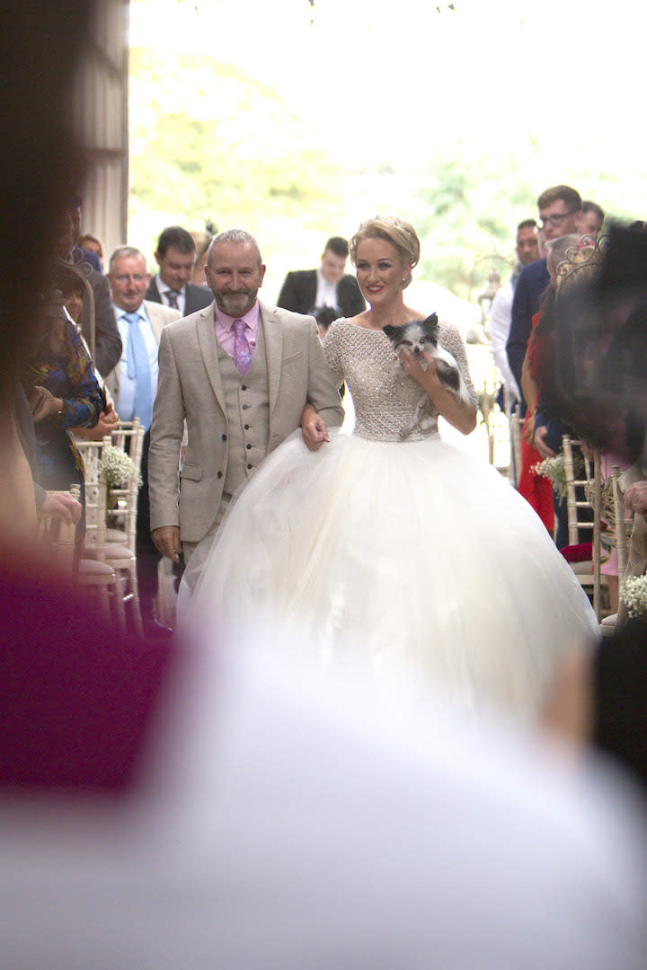 The bride walks down the aisle with her 17-year-old pooch, Louisa, in her arms [Photo: Caters]