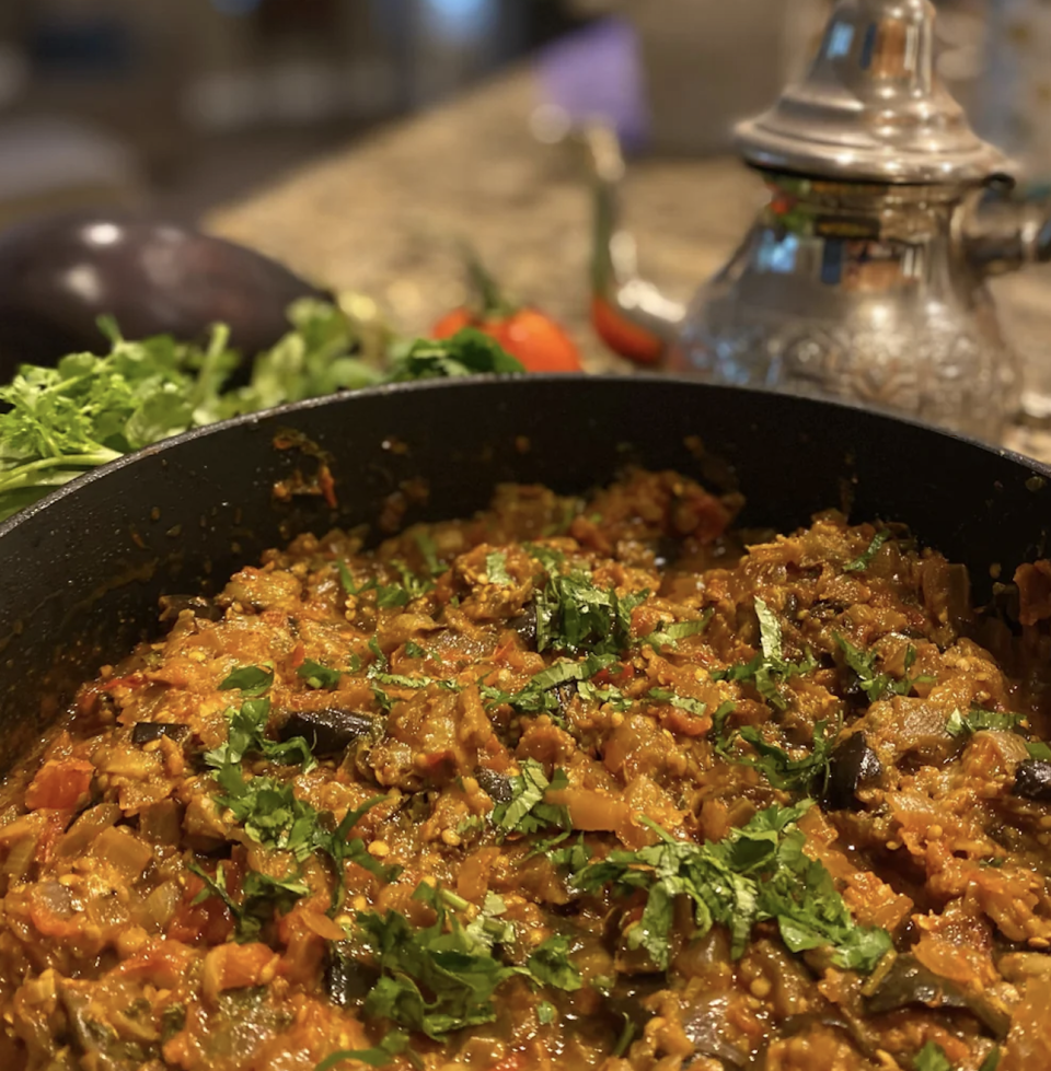 Pan of cooked eggplant dish garnished with herbs, kitchen counter backdrop