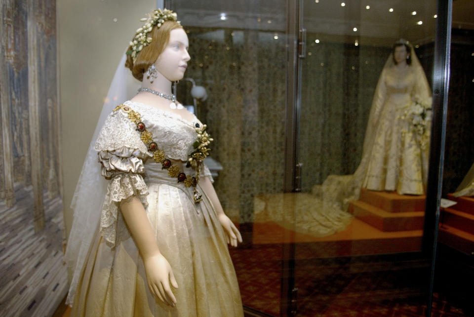 Two mannequins in a museum display wearing vintage bridal gowns with intricate lace and floral accessories