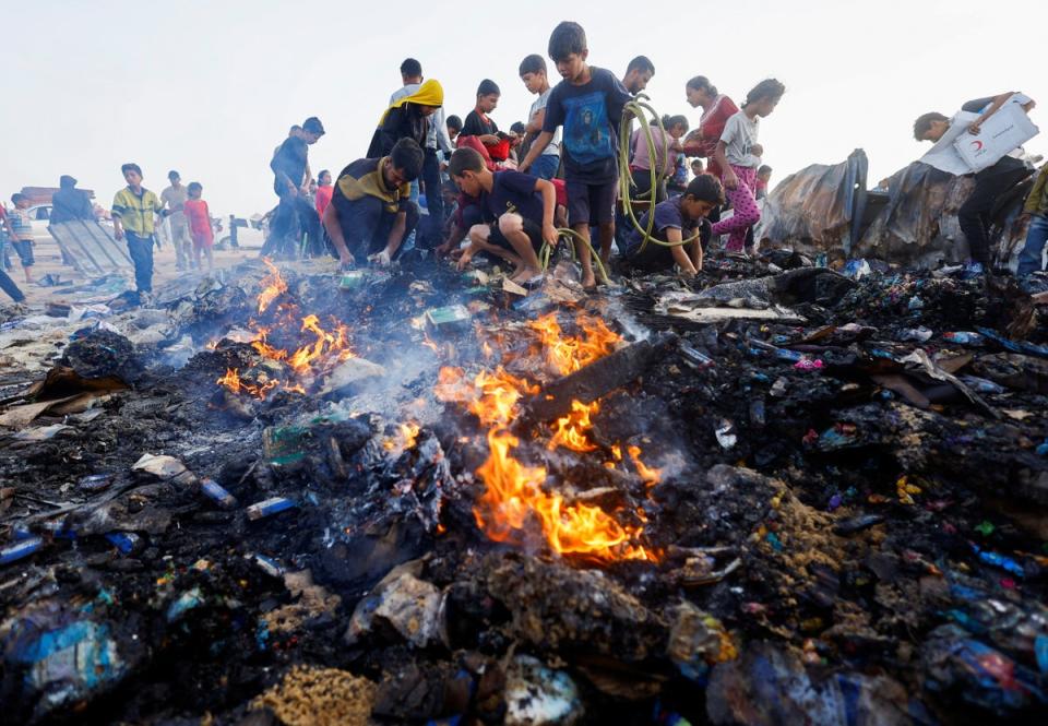 Palestinians search for food among burnt debris in the aftermath of an Israeli strike on an area designated for displaced people, in Rafah in the southern Gaza Strip, 27 May 2024 (Reuters)