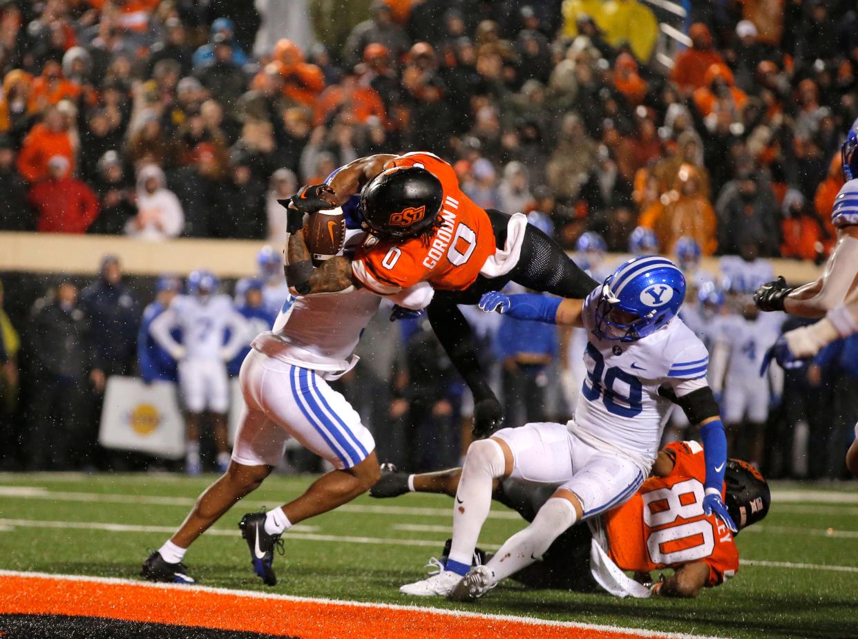 Nov 25, 2023; Stillwater, Oklahoma, USA; Oklahoma State's Ollie Gordon II (0) scores a touchdown in the second overtime as BYU's Eddie Heckard (5) and Crew Wakley (38) defend during the college football game between the Oklahoma State University Cowboys and the Brigham Young Cougars at Boone Pickens Stadium. Mandatory Credit: Sarah Phipps-USA TODAY Sports