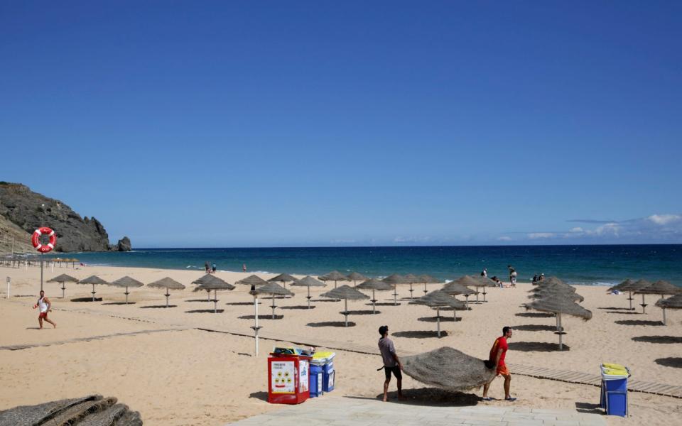 Two men set up sun umbrellas at the beach in Praia da Luz, in Portugal's Algarve coast - Armando Franca/AP