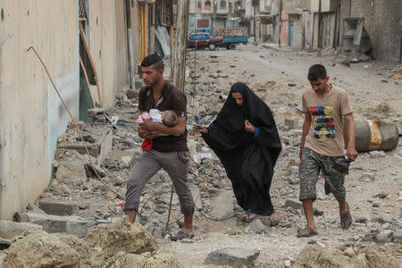 A displaced Iraqi man carries a child along a street covered in debris as the battle between the Iraqi Counter Terrorism Service and Islamic State militants continues nearby, in western Mosul, Iraq, April 23, 2017. REUTERS/Marko Djurica