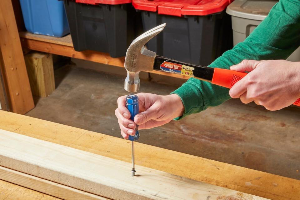 A person using a hammer and a handheld screwdriver to remove a stripped screw.