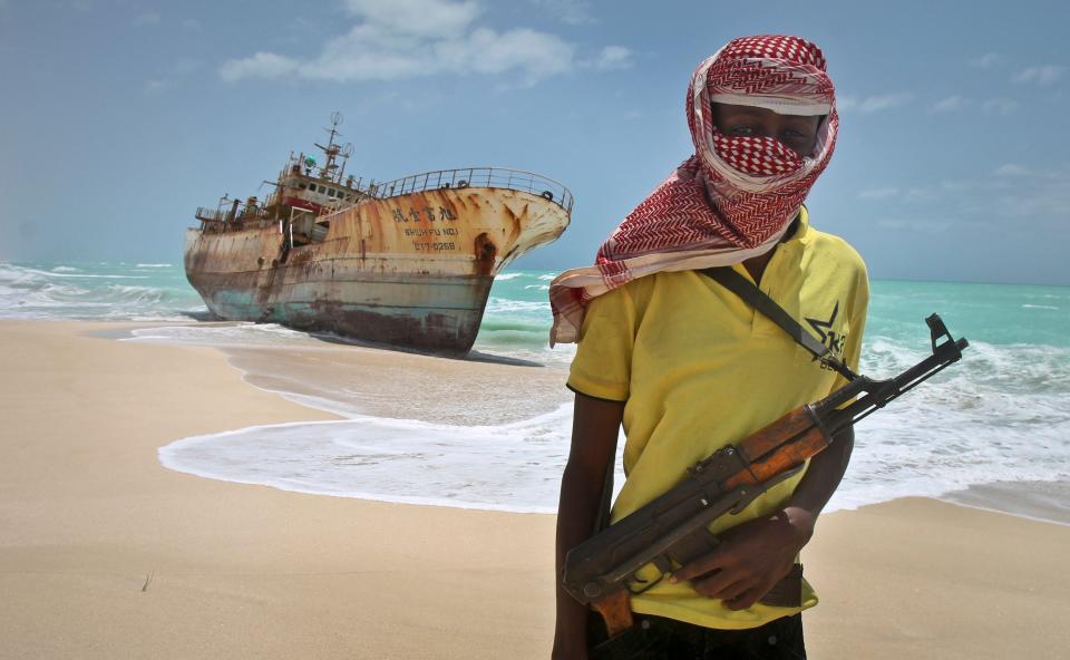 Sunday, Sept. 23, 2012 file photo, masked Somali pirate Hassan stands near a Taiwanese fishing vessel that washed up on shore after the pirates were paid a ransom and released the crew, in the once-bustling pirate den of Hobyo, Somalia.