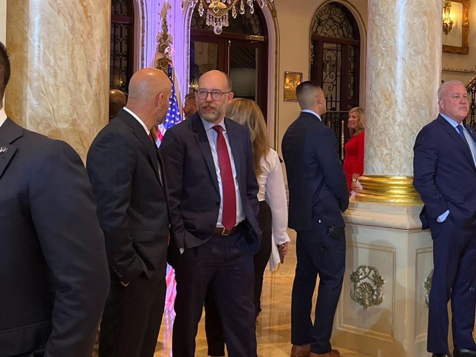 Men in blue and black suits at Mar-A-Lago gold ballroom