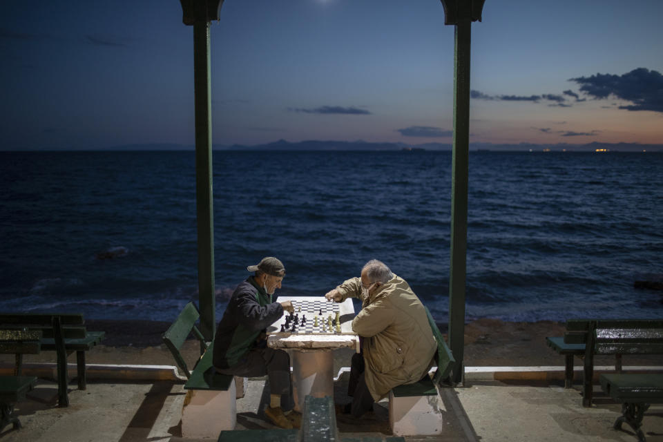 Two men wearing protective face masks play chess in Alimos, a seaside suburb of Athens, on Tuesday, April 20, 2021. (AP Photo/Petros Giannakouris)