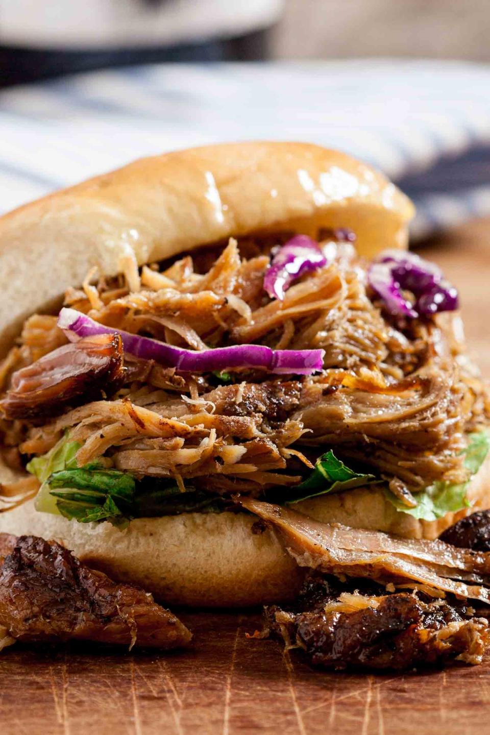 Close-up of a pulled pork sandwich with shredded pork, lettuce, and purple cabbage on a wooden surface