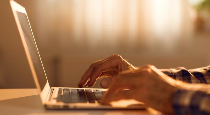 This image shows a retiree typing on a laptop