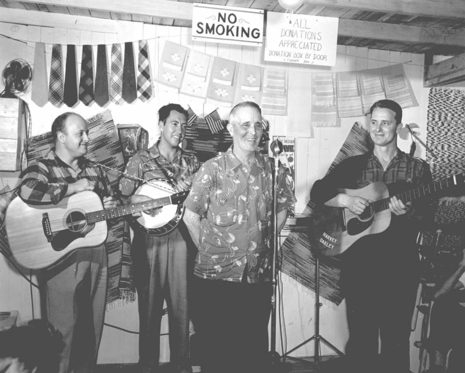 In the 1930s, Wiley Oakley and his wife Rebecca Ann opened the Wiley Shop in Gatlinburg, Tennessee. Here, Wiley entertains from behind a microphone inside the shop. The couple’s son Harvey is on the right playing the guitar bearing his name.