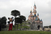 FILE - In this June 8, 2018 file photo, a person dressed as Mickey Mouse poses in front of the castle of Sleeping Beauty at Disneyland Paris, in Chessy, France, east of Paris. The French tourist industry received a further boost Wednesday, July 15, 2020 with the partial reopening of Disneyland Paris and the opening up of the top floor of the Eiffel Tower. Disneyland Paris, Europe’s most frequented theme park resort, is partially re-opening to the public, four months after it closed as a result of the coronavirus pandemic. (AP Photo/Francois Mori, File)