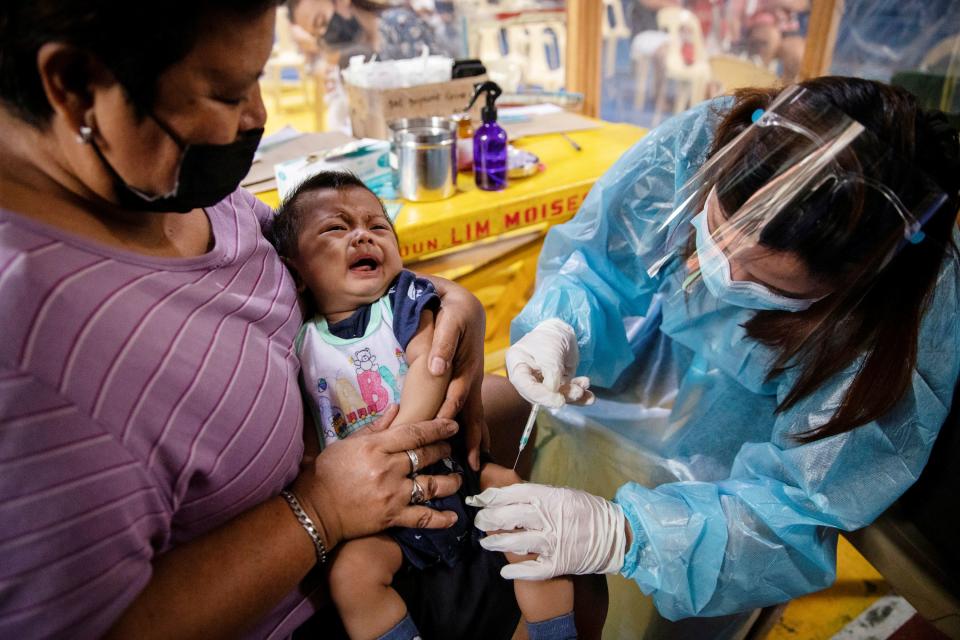 A nurse wearing personal protective equipment (PPE) for protection against the coronavirus disease (COVID-19) gives routine vaccines to a baby held by his mother in a local health center in Manila, Philippines January 27, 2021. Picture taken January 27, 2021. REUTERS/Eloisa Lopez