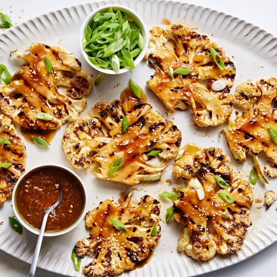 grilled teriyaki cauliflower steaks on a platter with more teriyaki sauce and scallions