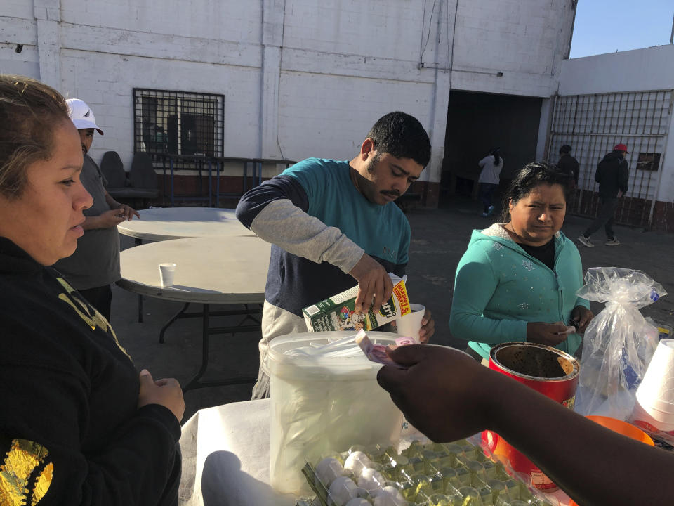 In this Jan. 11, 2020, photo, Joel Caceres, center, pours milk in his coffee as other asylum seekers at a migrant shelter purchase food in Mexicali, Mexico. Caceres, from Honduras, is seeking asylum in San Diego with his wife and two sons. Illegal border crossings have plummeted as the Trump administration has extended a policy to make asylum seekers wait in Mexico for court hearings in the U.S. (AP Photo/Elliot Spagat)