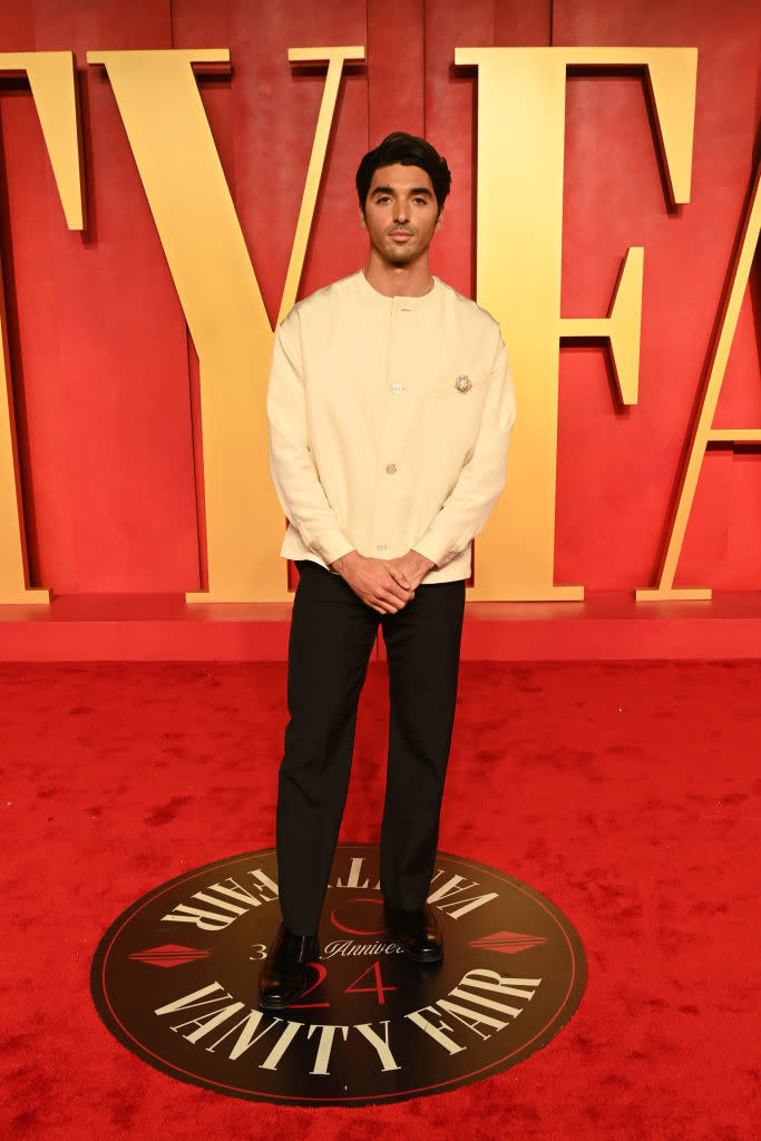 Man in a chic cream jacket and black trousers poses on a Vanity Fair event carpet
