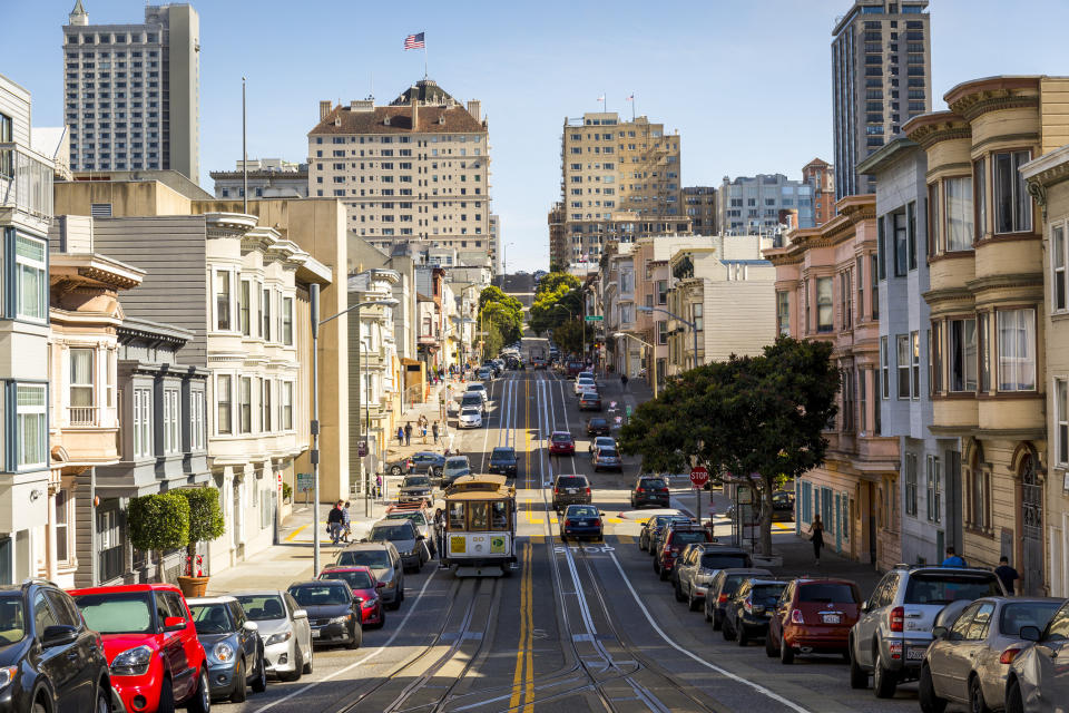 A wide residential street lined with a cars and a trolley running down the middle