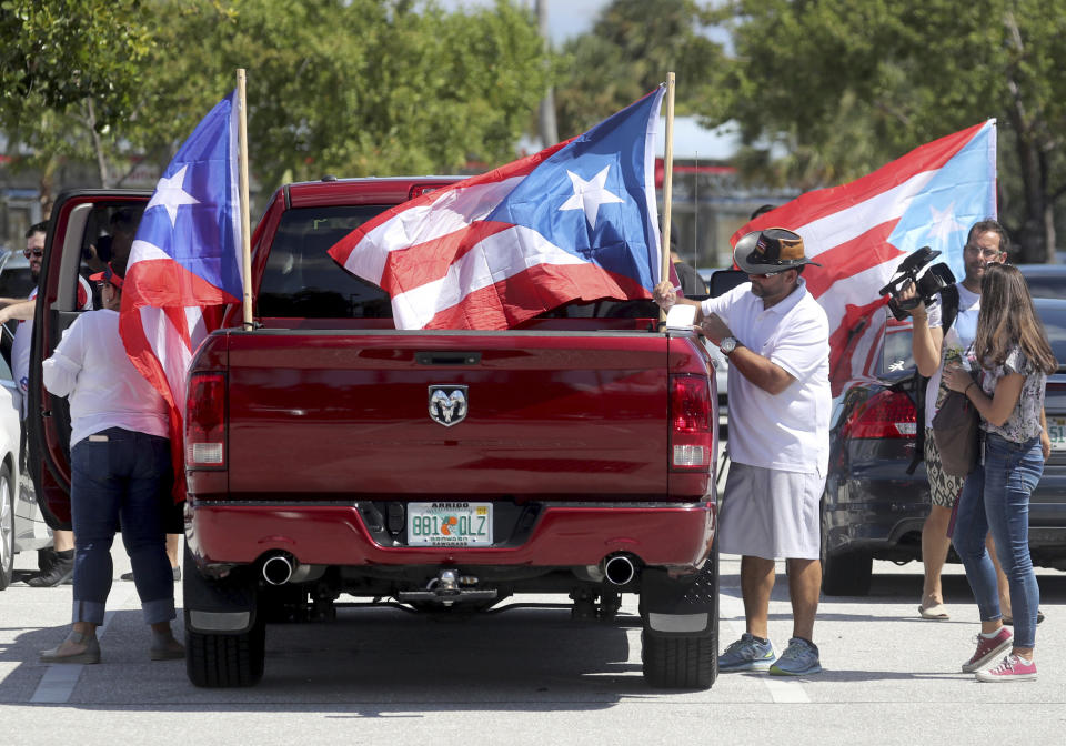 People gather in the parking lot and get ready to head to West Palm Beach for a protest, Saturday, Sept. 22, 2018 in Hollywood, Fla. Activists marking the one-year anniversary of Hurricane Maria's devastation of Puerto Rico are staging a rally and caravan focused on President Donald Trump's Mar-a-Lago resort in Florida. (Mike Stocker /South Florida Sun-Sentinel via AP)