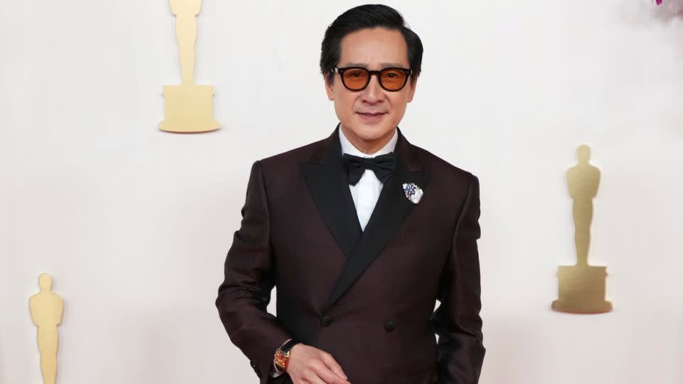 Ke Huy Quan wore a double-breasted deep red Giorgio Armani suit styled with amber-tinted shades. - Jordan Strauss/Invision/AP