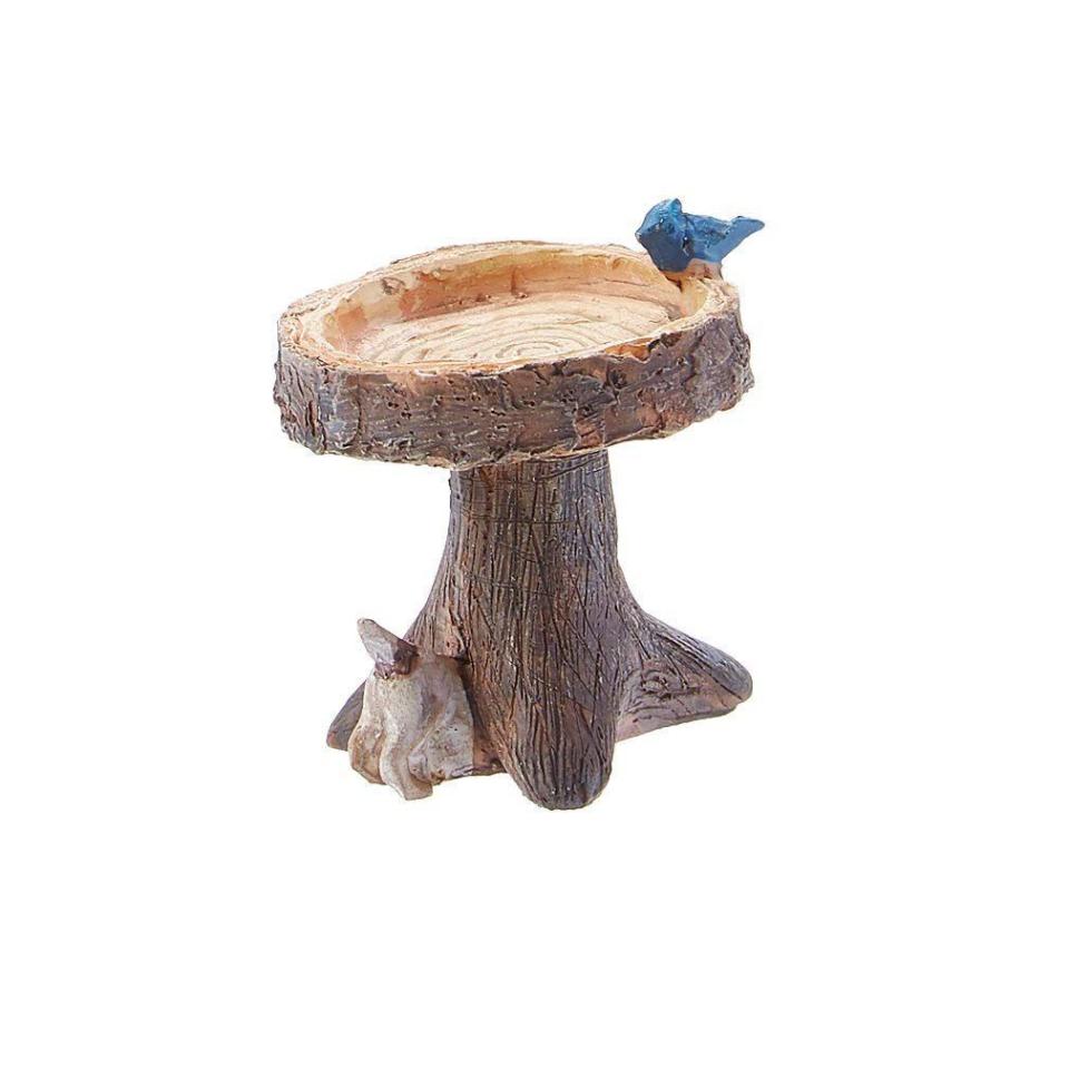 Miniature wood-finish birdbath with blue bird on top and dog digging under trunk